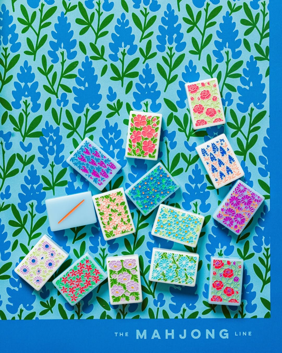 A set of colorful mahjong tiles arranged on a blue and green floral patterned background Mahjong Mat made by the Mahjong Line at The Queen's Mahjery in Charlotte, NC.