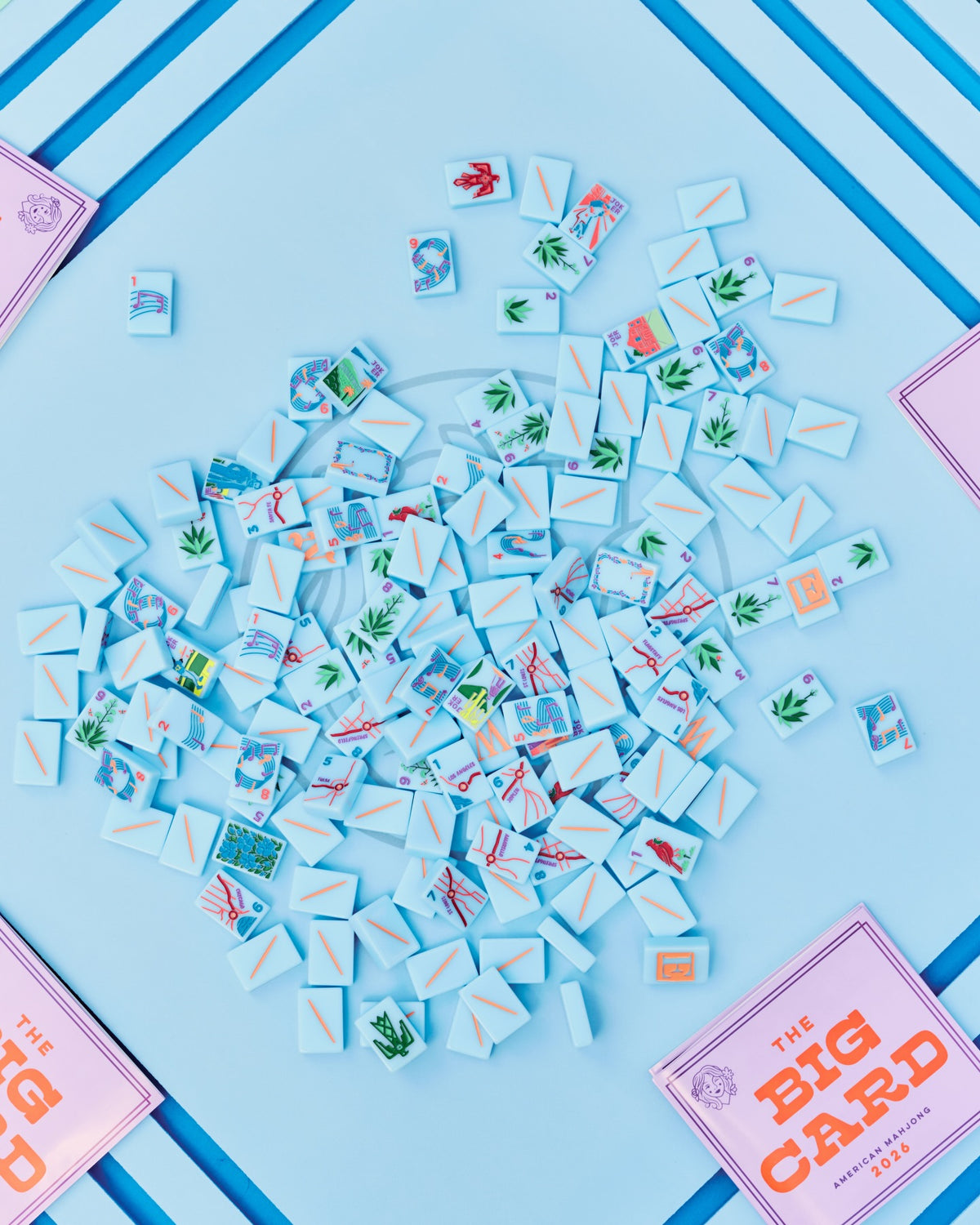 A top-down view of a Mahjong board at The Queen's Mahjery in Charlotte, NC, showing 'The Big Card' with many small Mahjong tiles scattered in the center on a light blue background with blue stripes. 
